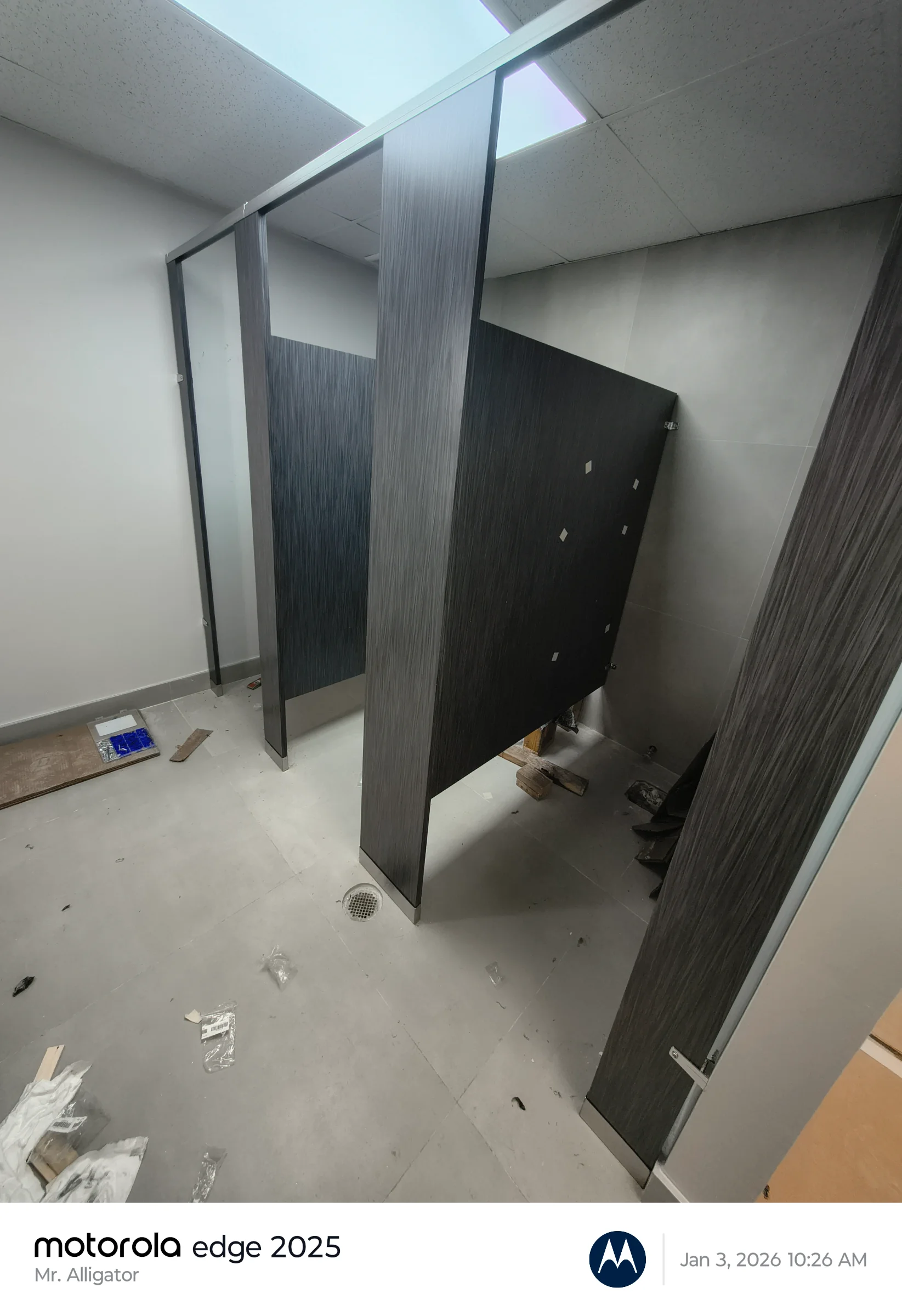 Installation phase of dark-finished commercial restroom stall partitions and tile flooring layout.